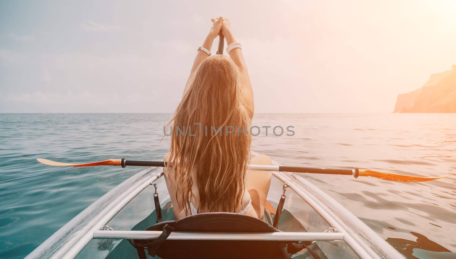 Woman in kayak back view. Happy young woman with long hair floating in transparent kayak on the crystal clear sea. Summer holiday vacation and cheerful female people having fun on the boat.