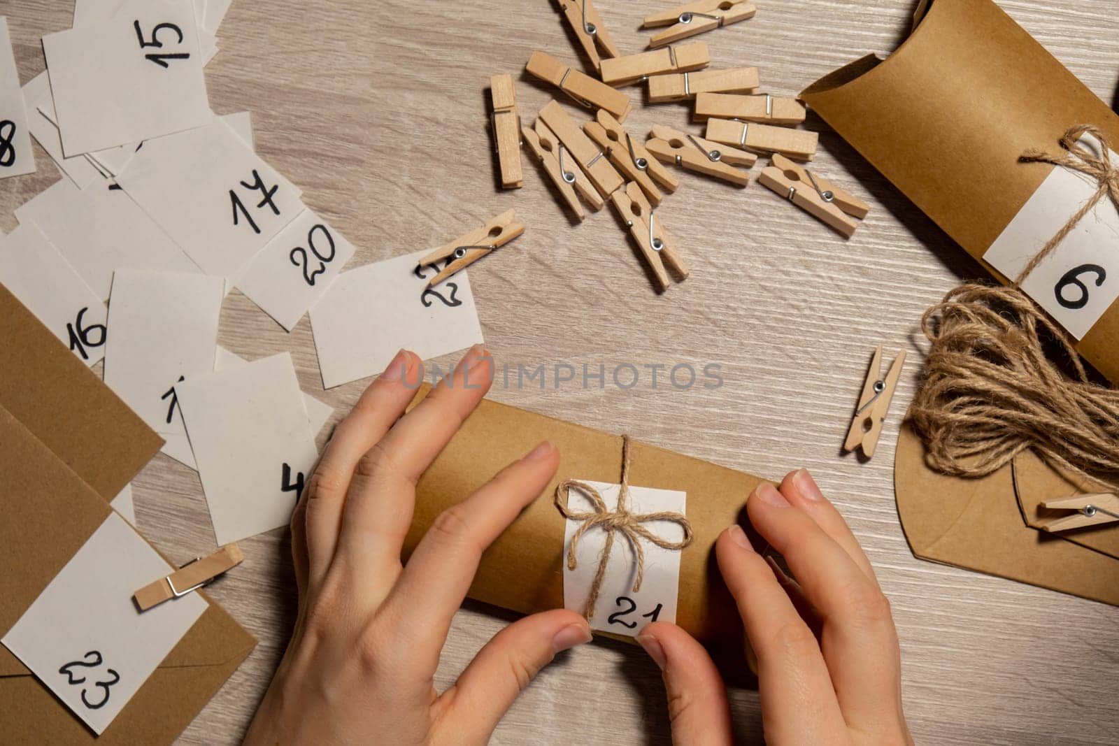 Unrecognizable young woman sticks number on craft bag, fastens with clothespin. Female making kraft paper for homemade advent calendar Made with your own hands step by step DIY crafts do it yourself. Preparation to christmas concept. Seasonal activities for children family winter holidays. Eco friendly presents gifts. open the package every day