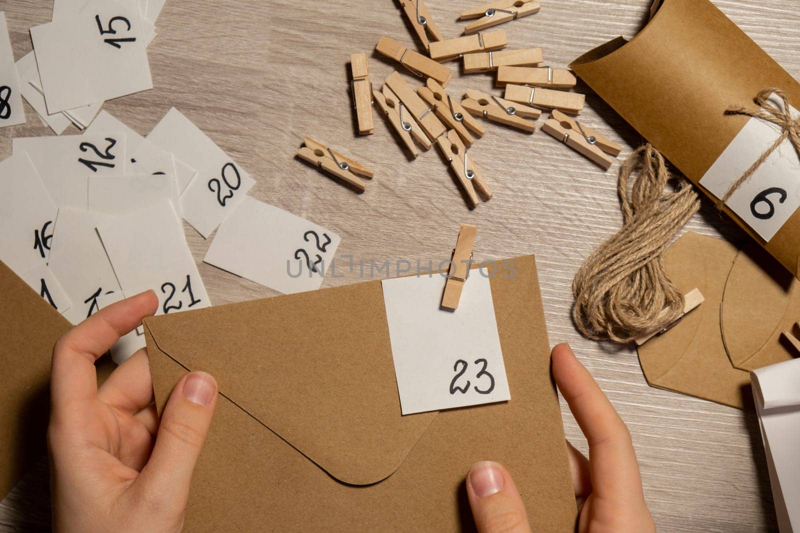 Unrecognizable young woman sticks number on craft bag, fastens with clothespin. Female making kraft paper for homemade advent calendar Made with your own hands step by step DIY crafts do it yourself. Preparation to christmas concept. Seasonal activities for children family winter holidays. Eco friendly presents gifts. open the package every day