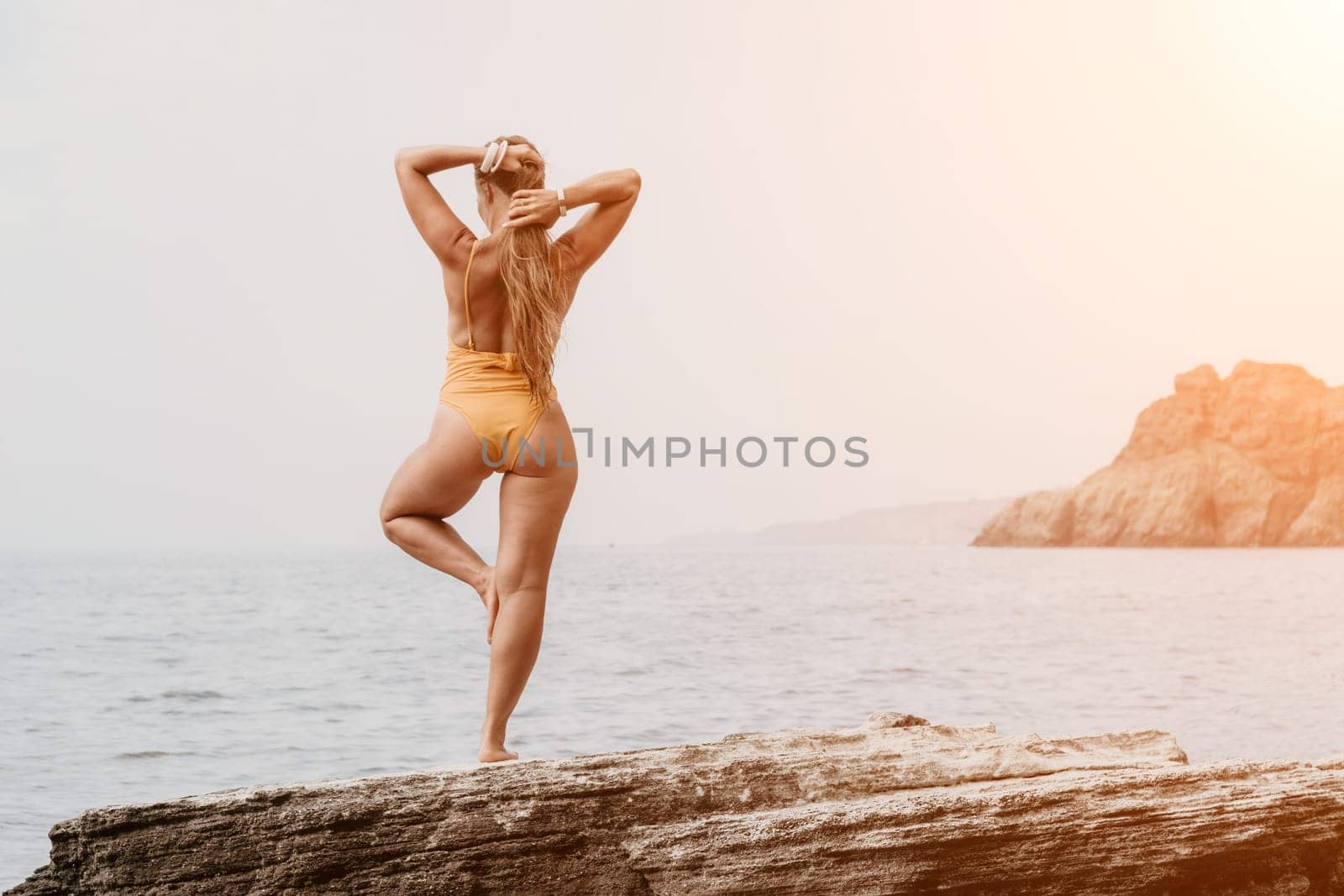 Woman meditating in yoga pose silhouette at the ocean, beach and rock mountains. Motivation and inspirational fit and exercising. Healthy lifestyle outdoors in nature, fitness concept.