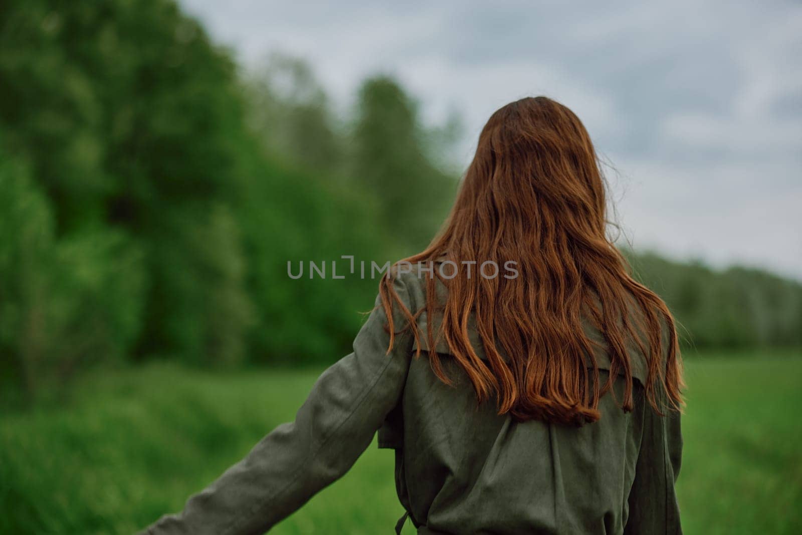 a woman with beautiful, well-groomed jumpy hair developing in the wind stands in a field. High quality photo