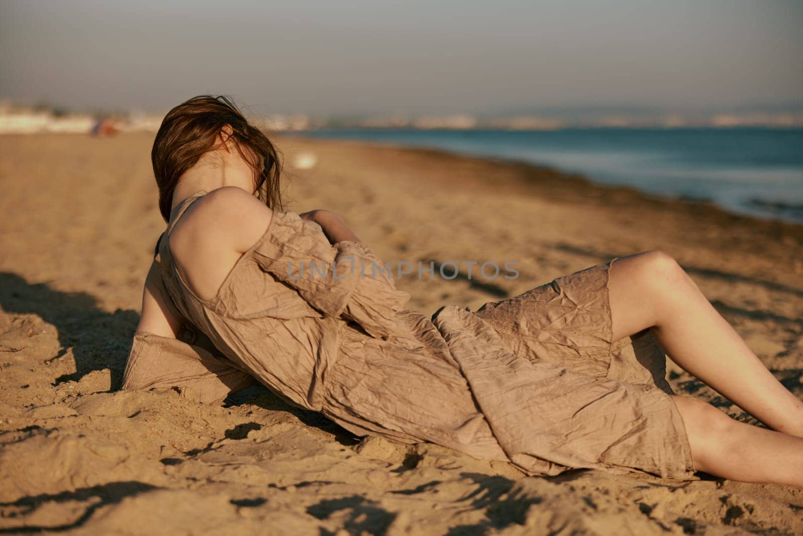 woman lies on the beach on a sunny day during sunset and turned her face away from the camera by Vichizh