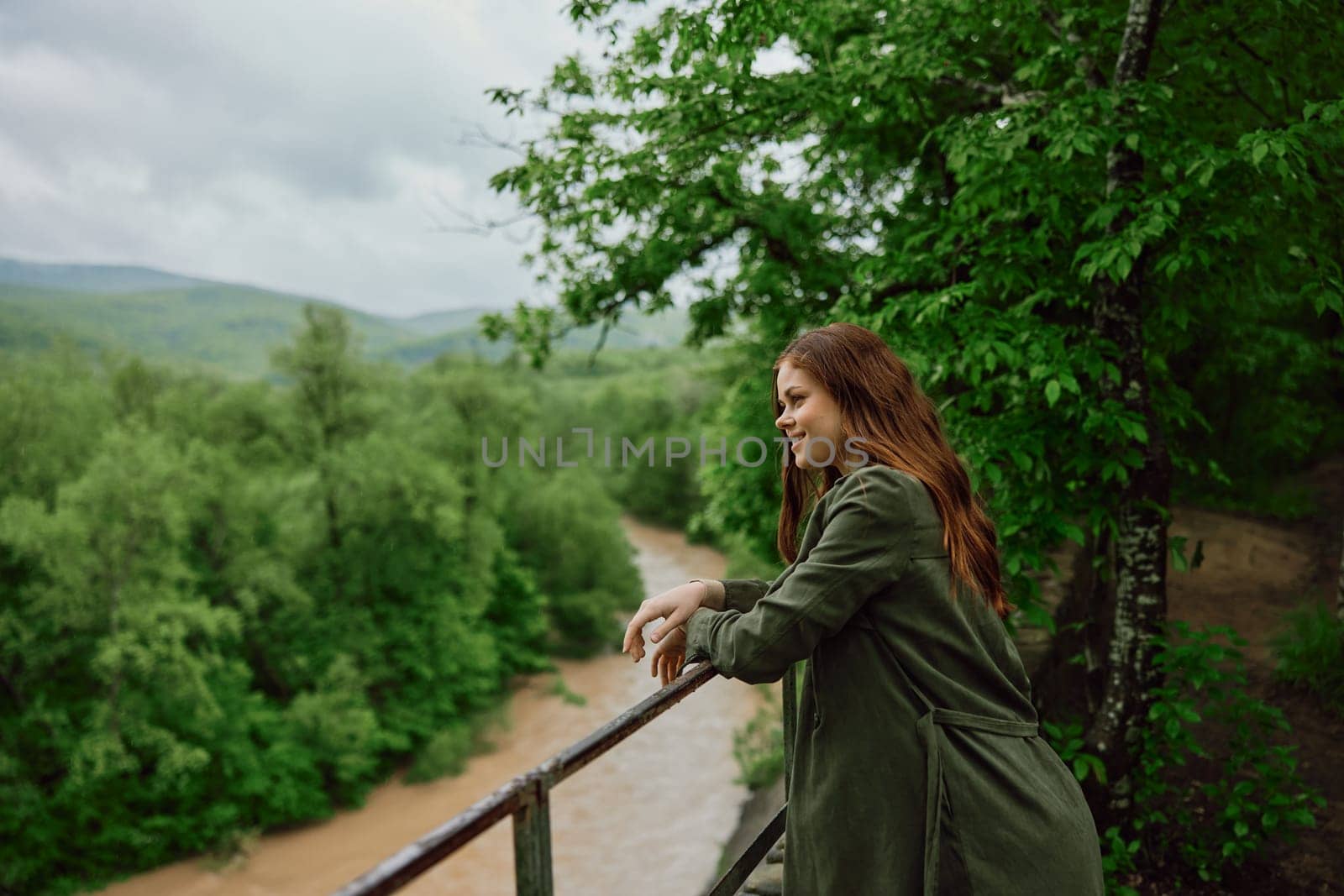 happy woman in a raincoat walks in the spring in the park near a stormy, mountain river by Vichizh