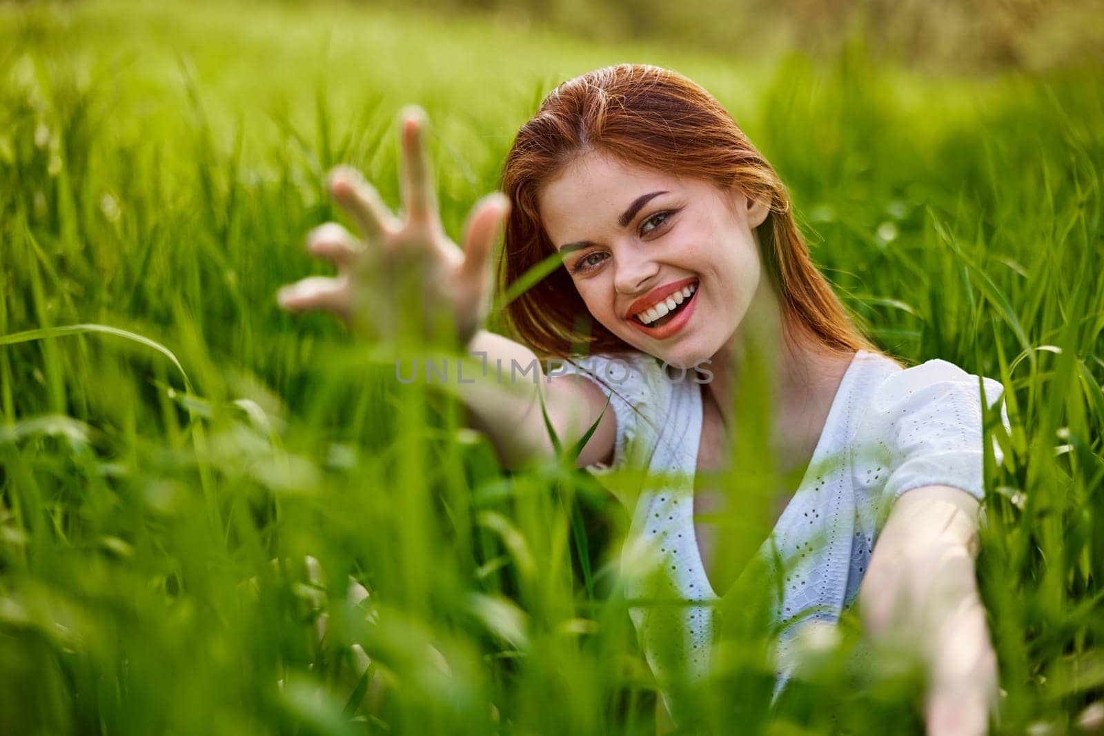 portrait of a broadly smiling woman sitting in tall grass and holding out her hands to the camera. High quality photo