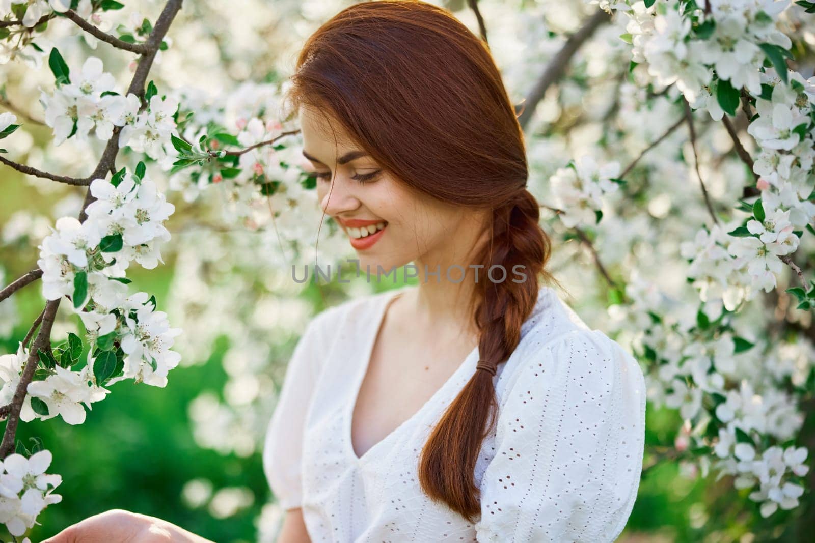 a beautiful woman in a light dress enjoys the spring while standing next to a flowering tree by Vichizh