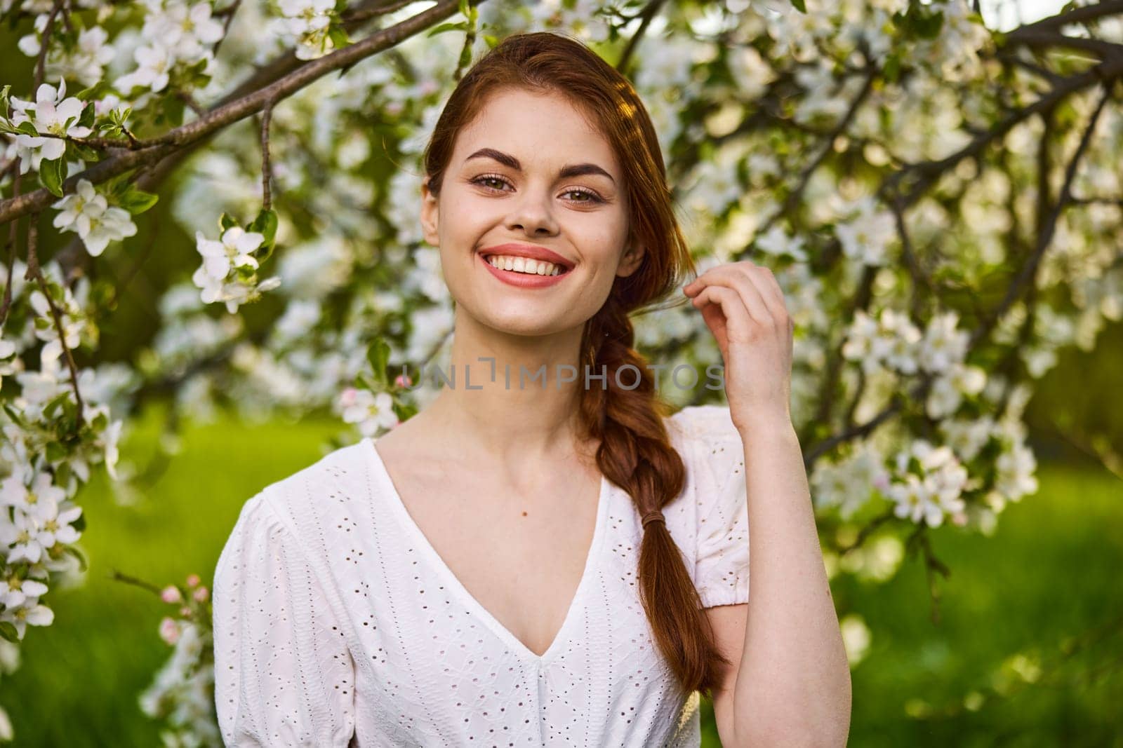 a joyful, carefree woman in a light dress stands against the background of a flowering tree by Vichizh
