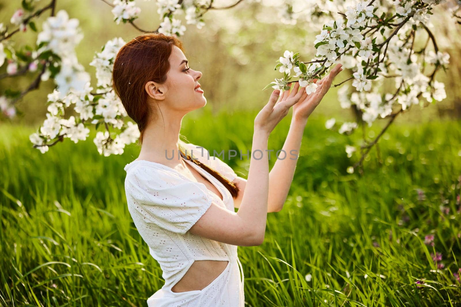 Young attractive woman with straight long hair standing in flowering Apple orchards. Beauty smiling woman looking at white flower. High quality photo