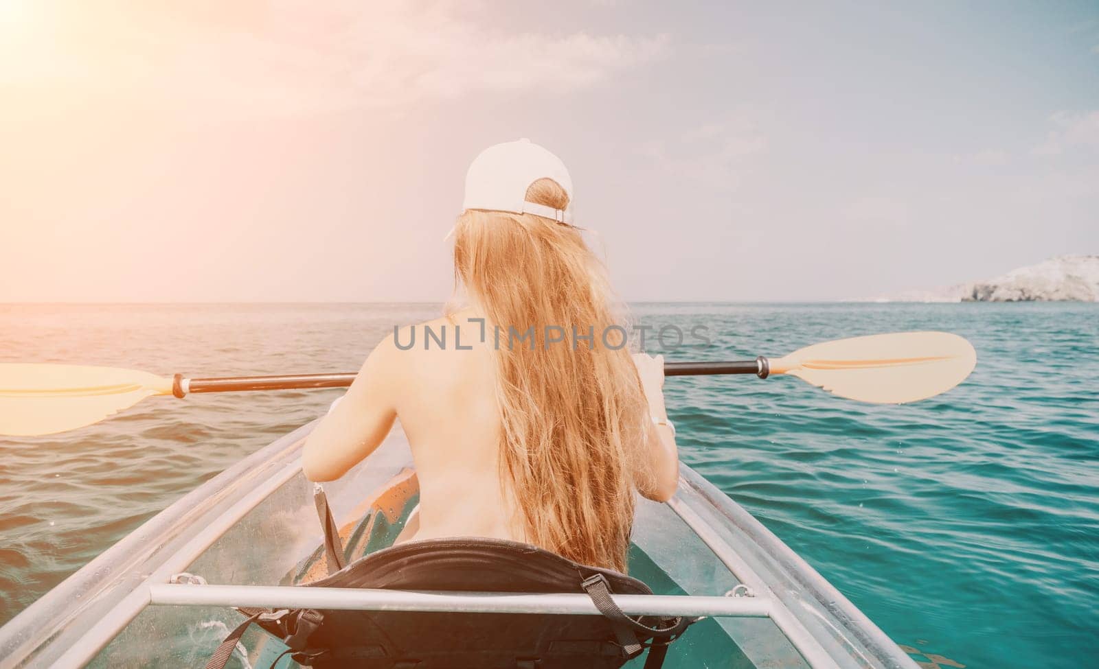 Woman in kayak back view. Happy young woman with long hair floating in transparent kayak on the crystal clear sea. Summer holiday vacation and cheerful female people having fun on the boat.