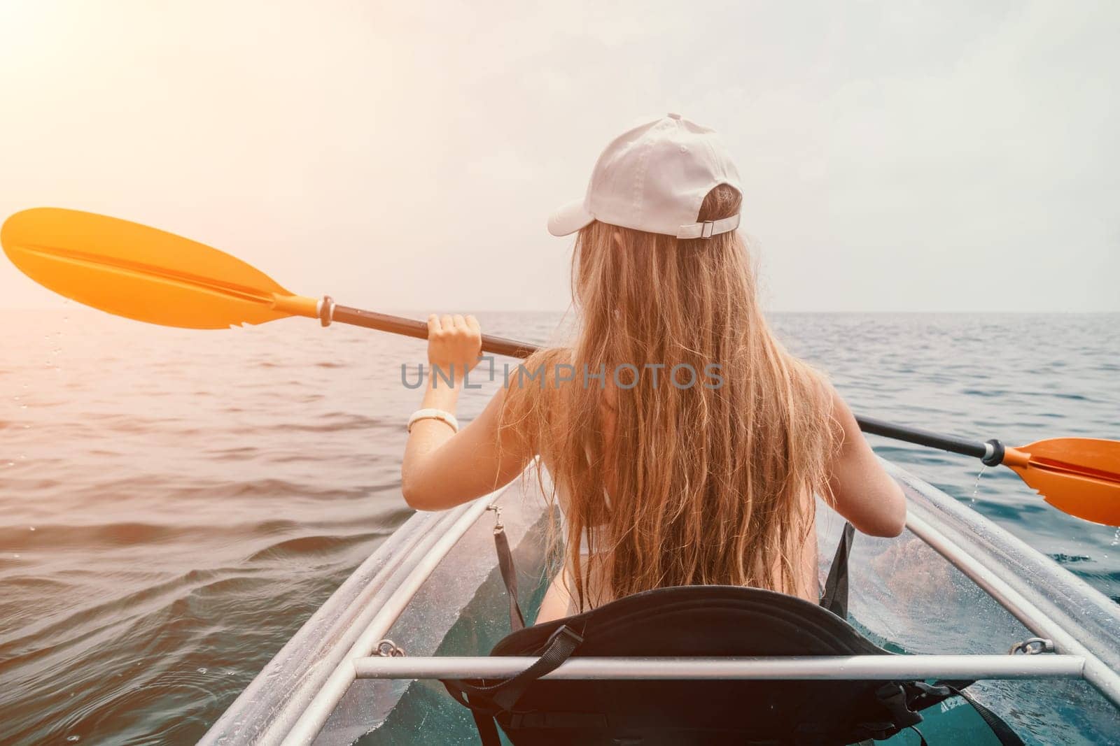 Woman in kayak back view. Happy young woman with long hair floating in transparent kayak on the crystal clear sea. Summer holiday vacation and cheerful female people relaxing having fun on the boat by panophotograph