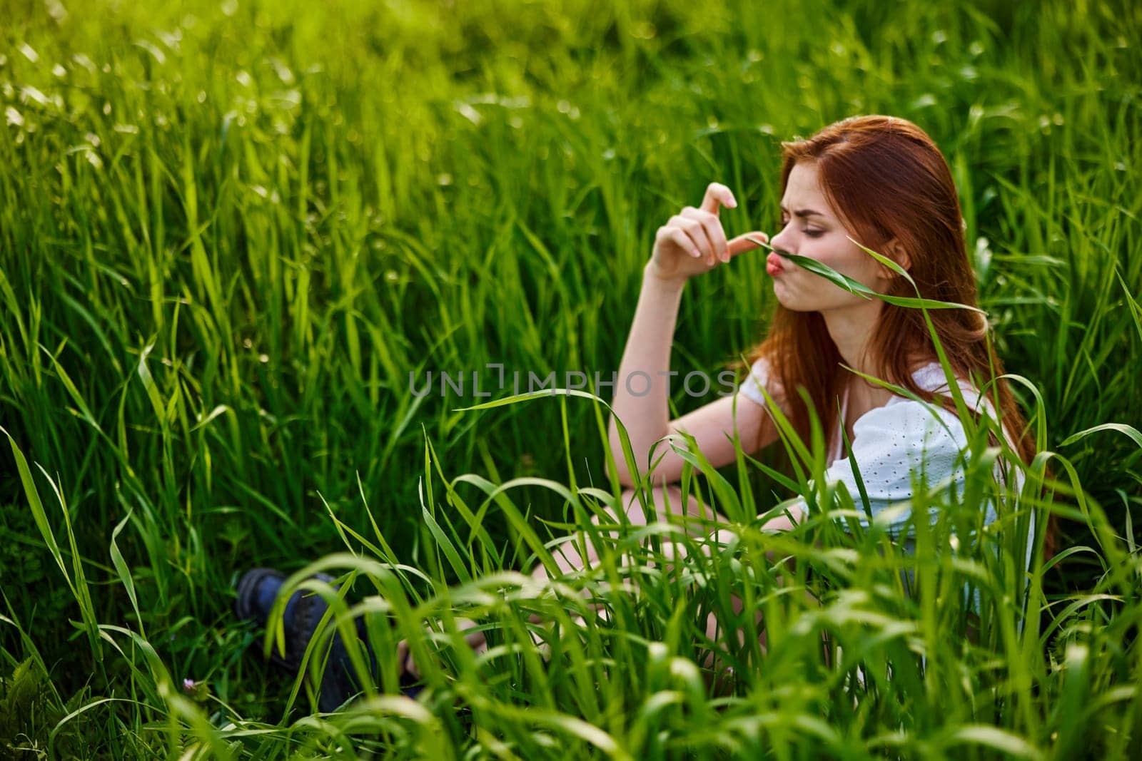 funny woman sits in high grass making herself a mustache from a blade of grass. High quality photo
