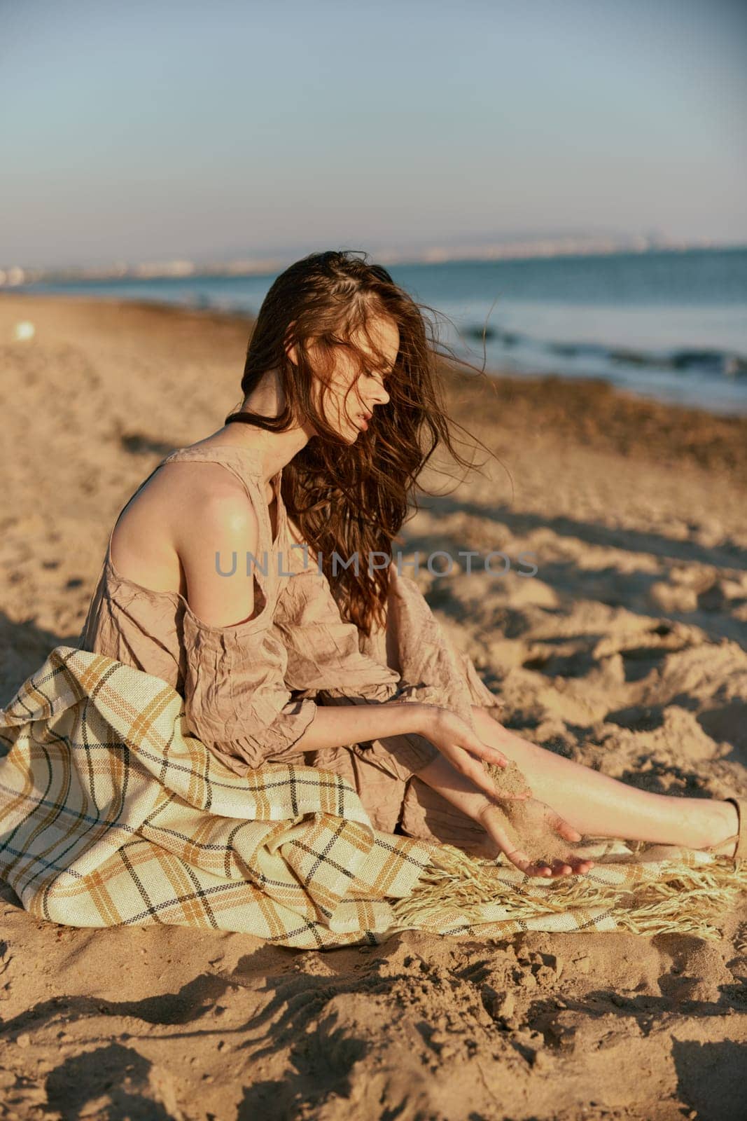 a woman near the sea sits on a blanket and looks into the distance in windy weather. High quality photo