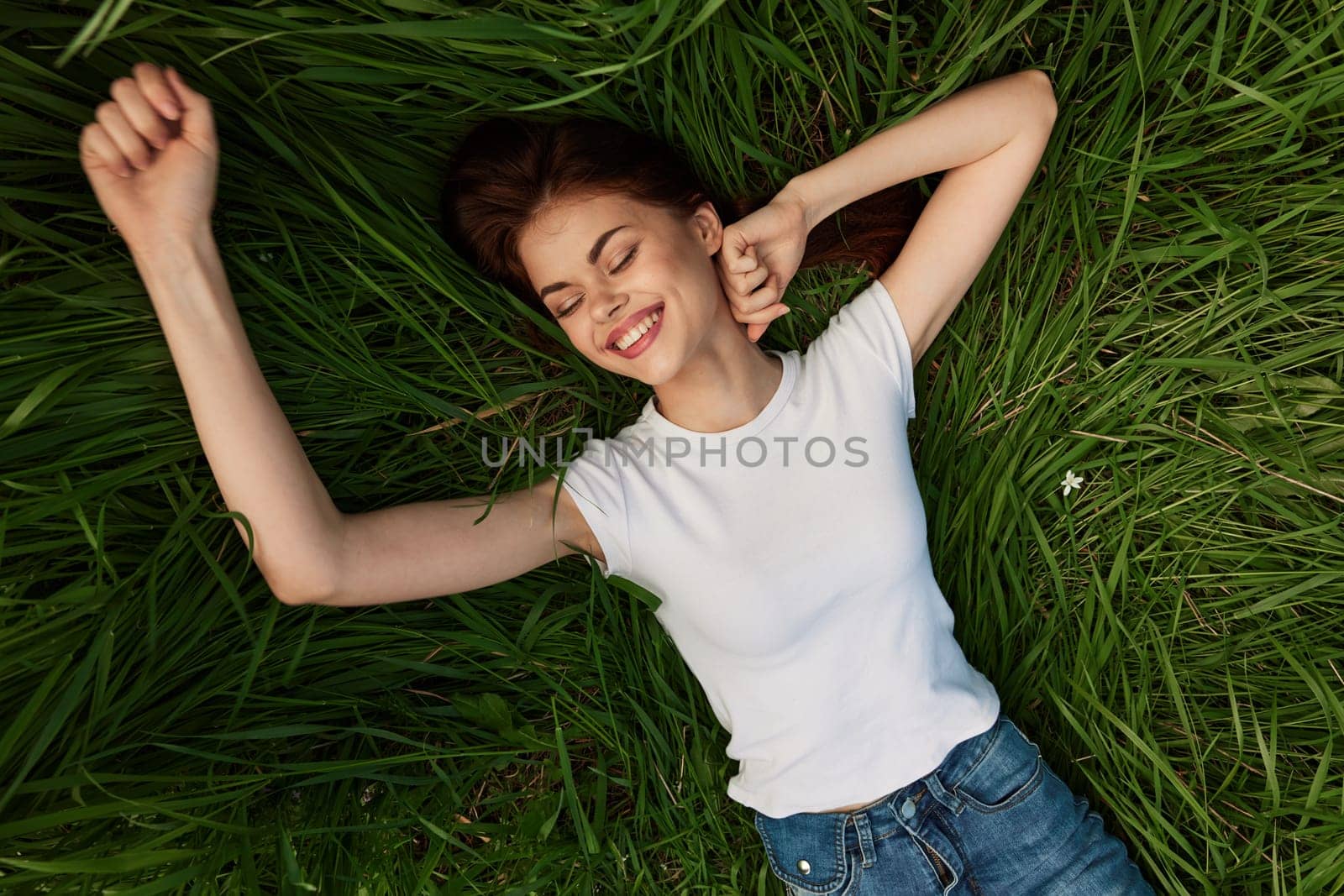 joyful, happy, carefree woman lies on the grass with her arms outstretched by Vichizh