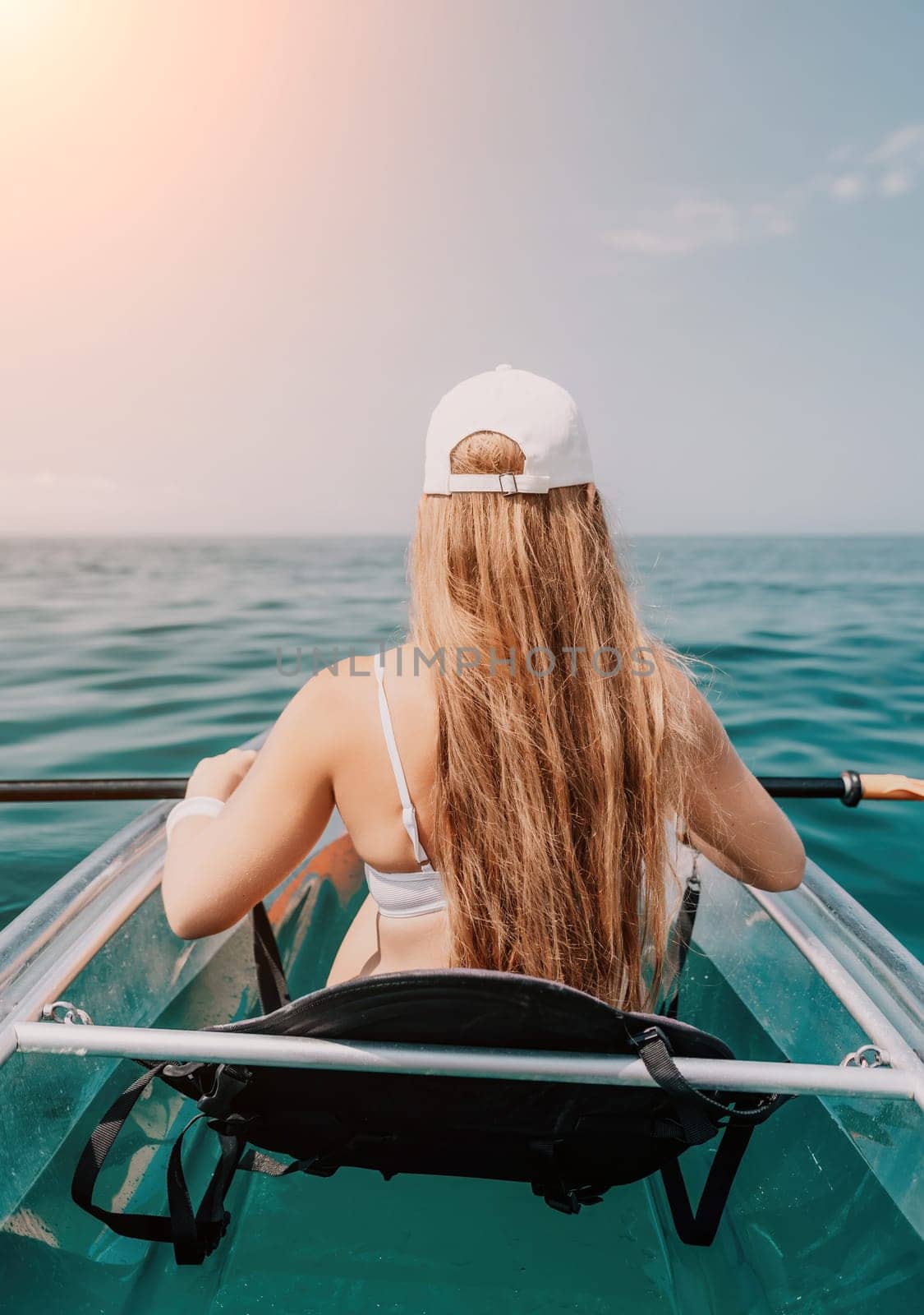 Woman in kayak back view. Happy young woman with long hair floating in transparent kayak on the crystal clear sea. Summer holiday vacation and cheerful female people having fun on the boat.