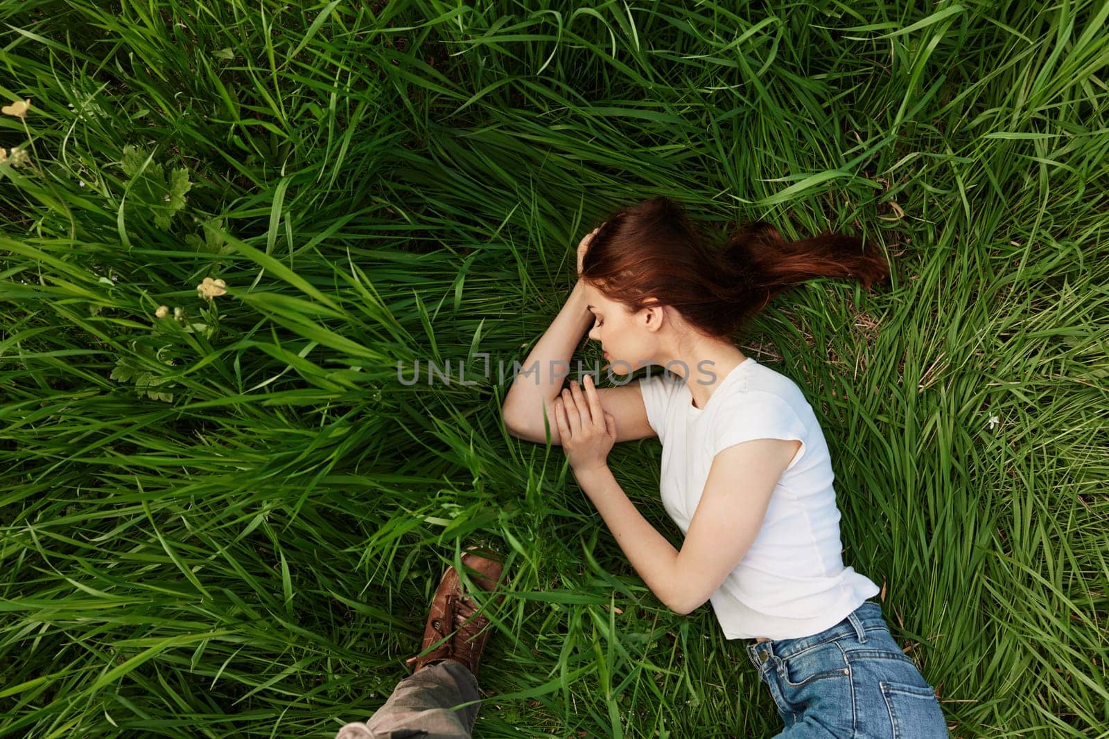 top view of a woman lying in tall green grass on a summer day by Vichizh