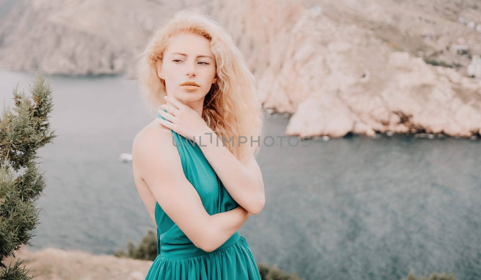 Side view a Young beautiful sensual woman in a mint long dress posing on a volcanic rock high above the sea during sunset. Girl on the nature on overcast sky background. Fashion photo