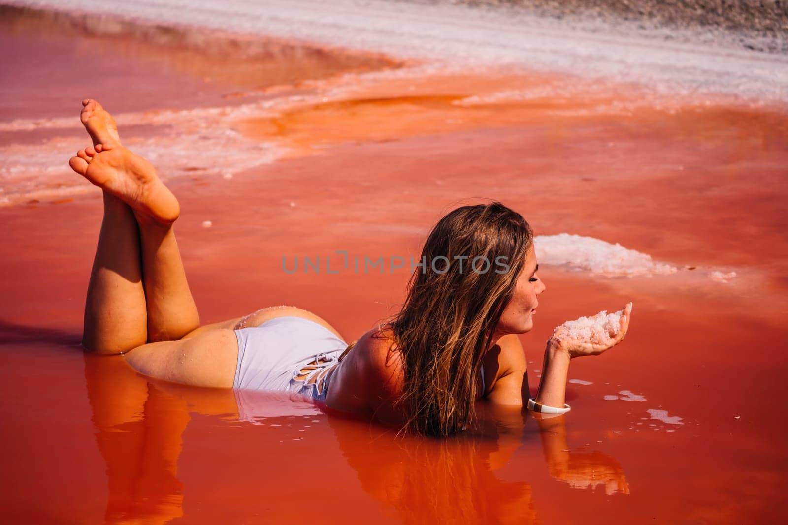 Young woman with long hair in pink salty lake with crystals of salt. Extremely salty pink lake, colored by microalgae with crystalline salt depositions. Spa, beauty and health care concept. by panophotograph