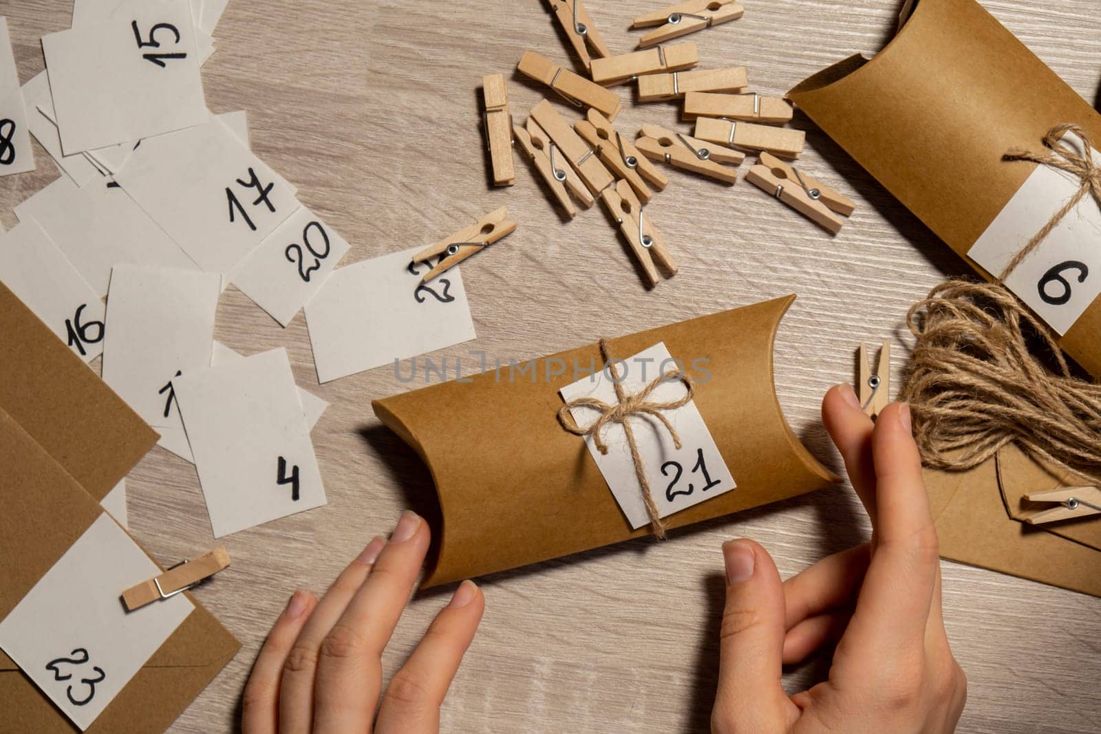 Unrecognizable young woman sticks number on craft bag, fastens with clothespin. Female making kraft paper for homemade advent calendar Made with your own hands step by step DIY crafts do it yourself. Preparation to christmas concept. Seasonal activities for children family winter holidays. Eco friendly presents gifts. open the package every day