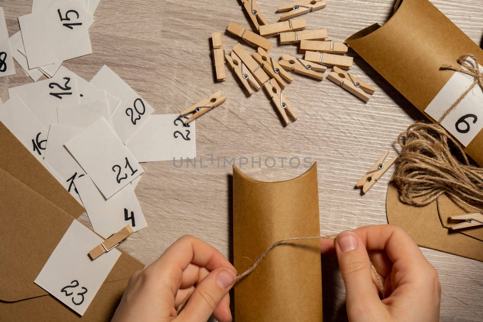 Unrecognizable young woman sticks number on craft bag, fastens with clothespin. Female making kraft paper for homemade advent calendar Made with your own hands step by step DIY crafts do it yourself. Preparation to christmas concept. Seasonal activities for children family winter holidays. Eco friendly presents gifts. open the package every day