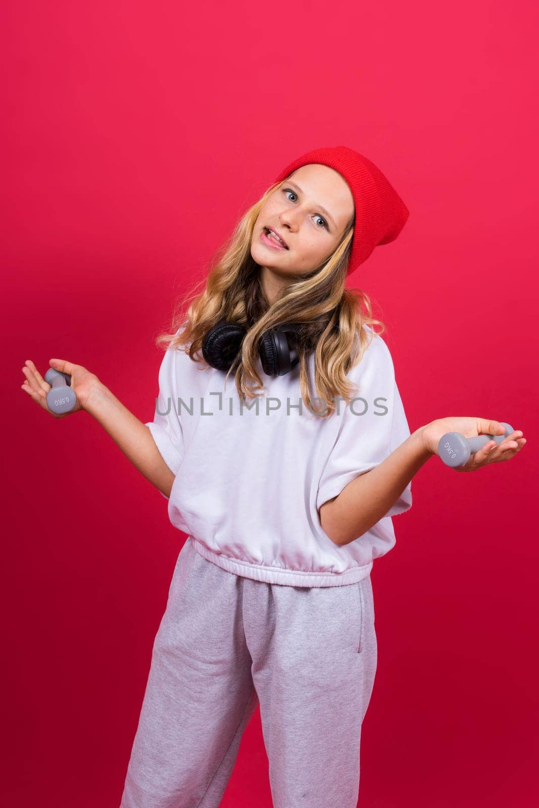 Kid girl doing fitness exercises with dumbbells on a red background