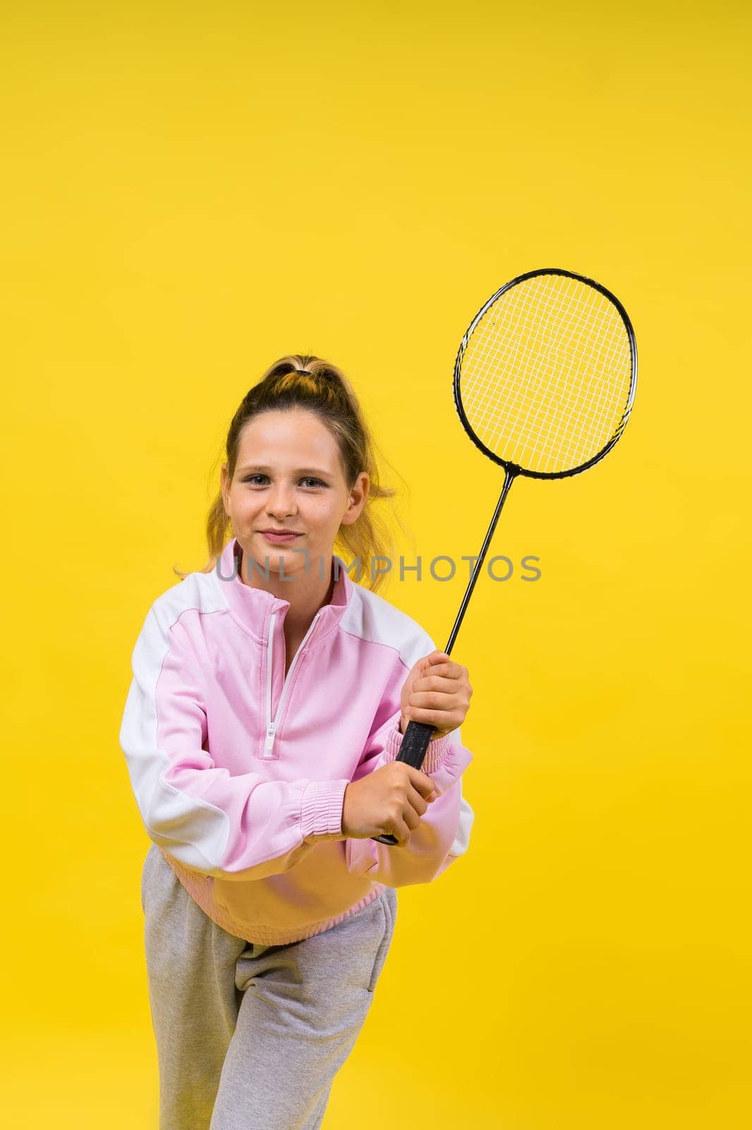 Full length studio photo of ten year old girl holding badminton racket and isolated on yellow. by Zelenin