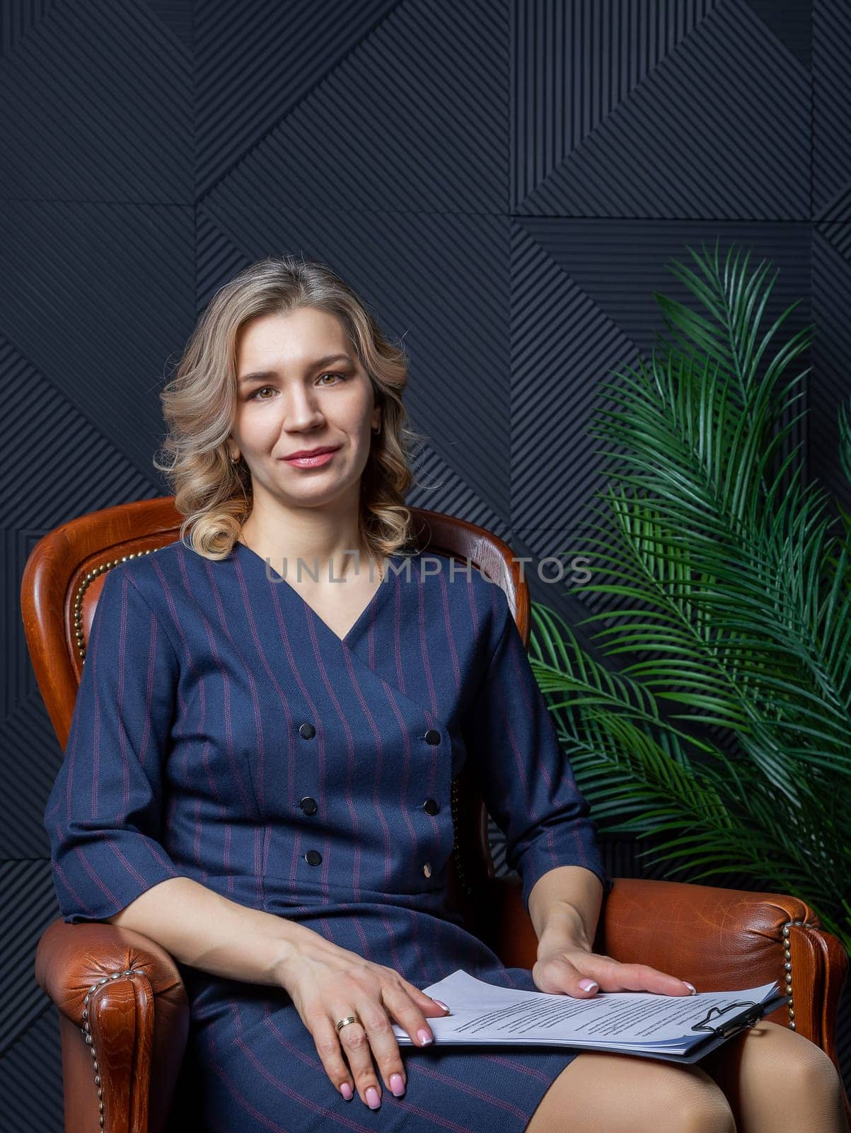 Portrait of a successful female psychologist in her office, notebook in hand, in her chair