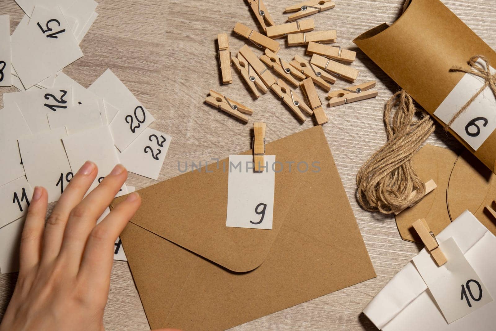 Unrecognizable young woman sticks number on craft bag, fastens with clothespin. Female making kraft paper for homemade advent calendar Made with your own hands step by step DIY crafts do it yourself. Preparation to christmas concept. Seasonal activities for children family winter holidays. Eco friendly presents gifts. open the package every day