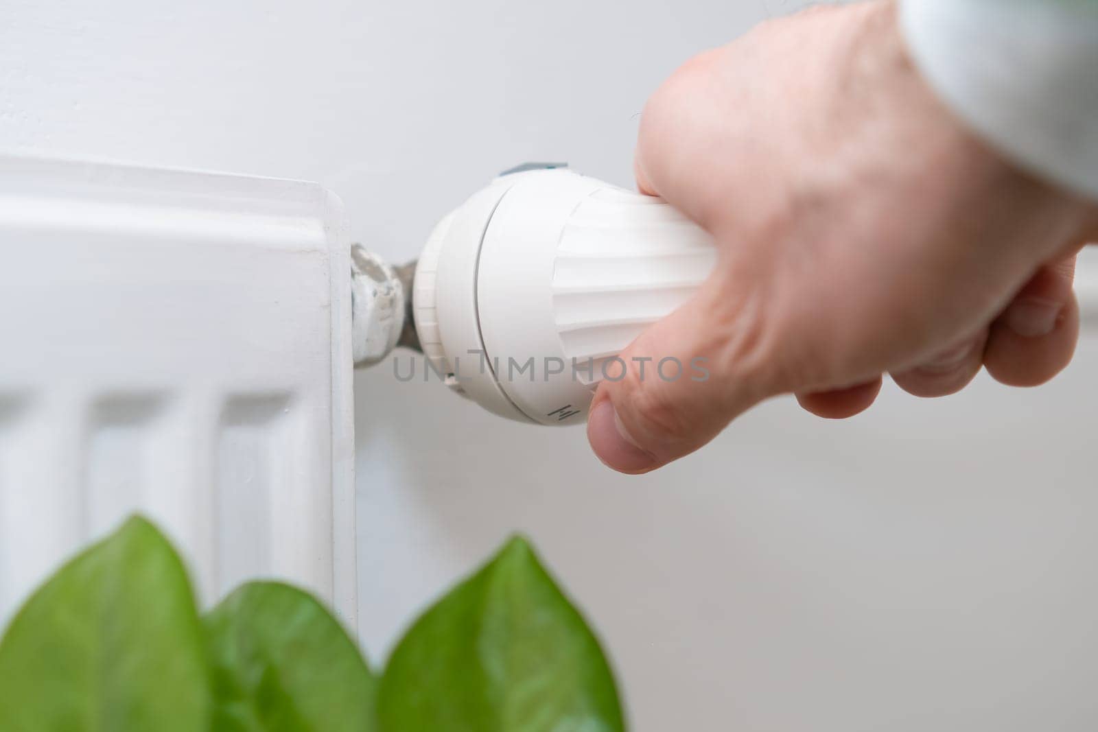 Man hand regulates temperature knob of the heating radiator to reduce heating costs.