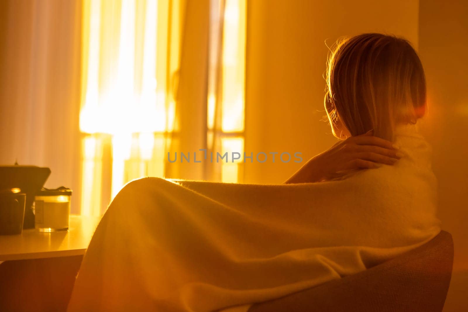 Romantic girl wrapped in the blanket, sitting in the living room and enjoys sunset in the window by vladimka