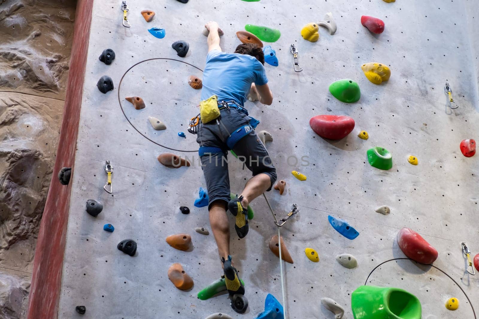 The climber trains on the artificial rock wall with insurance in bouldering gym, April 2022, Prague, Czech Republic.