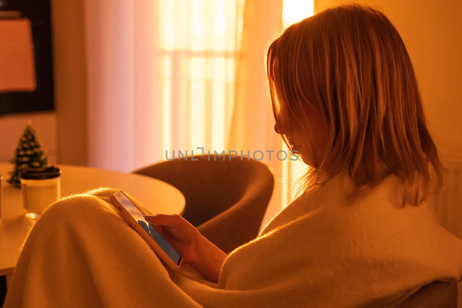 Woman relaxing and using a smartphone in cozy atmosphere in the kitchen with amazing sunlight from the window