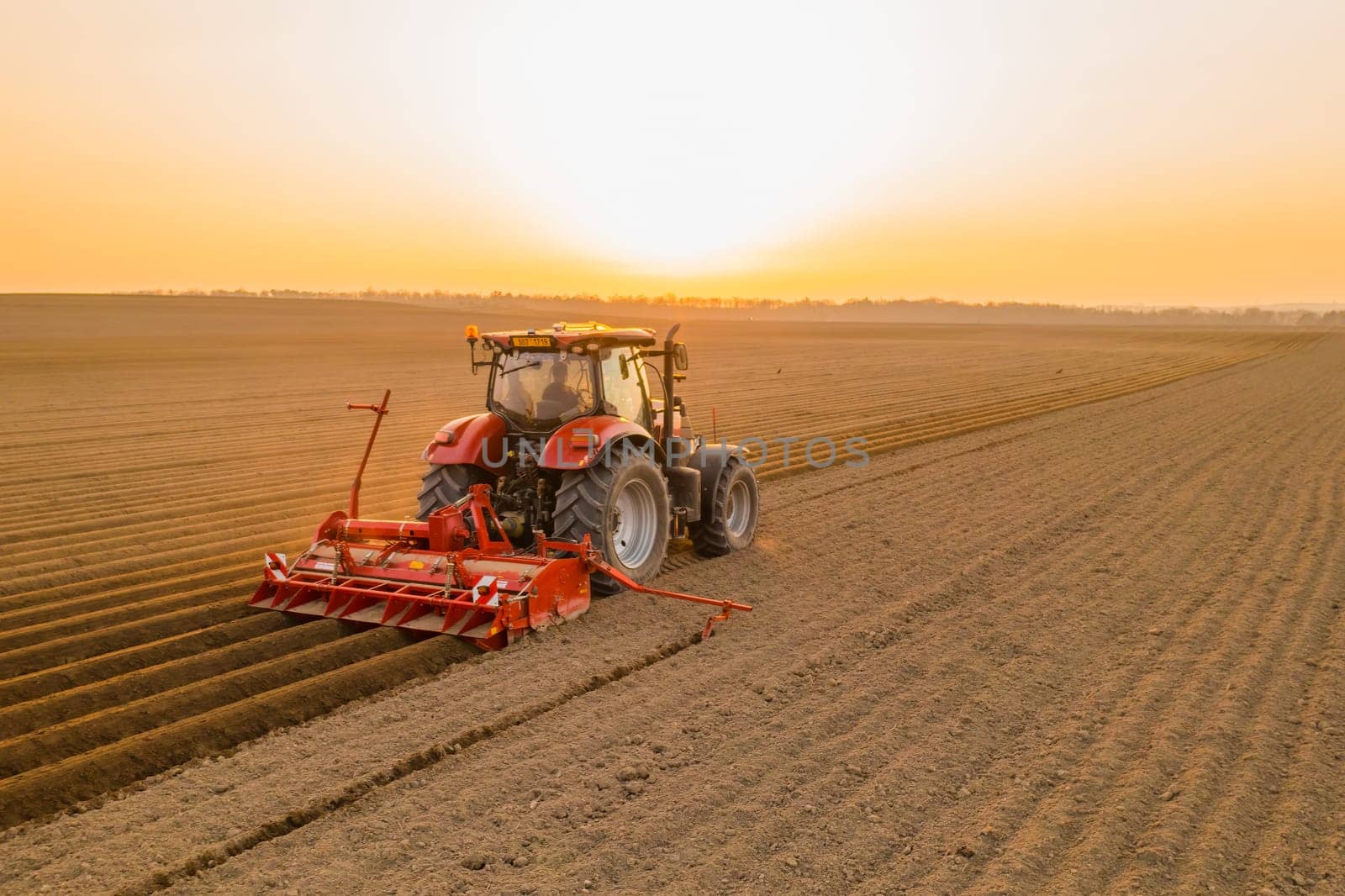 PRAGUE , CZECH REPUBLIC - MARCH 18 2022: Modern tractor cultivates soil in field on agricultural farm at bright sunset. Powerful machine works dragging plow behind at rural site in evening