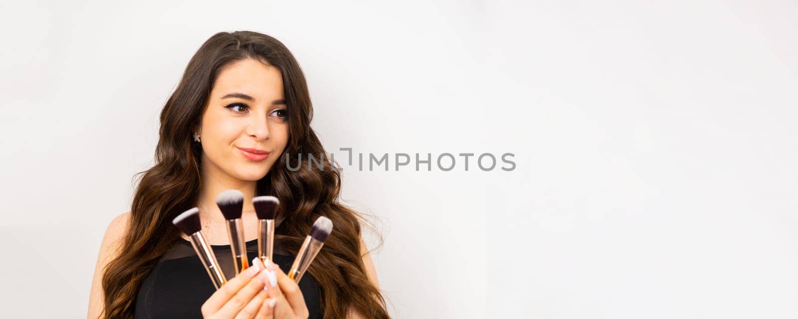 Beautiful woman with makeup brushes on the white background with copy space.