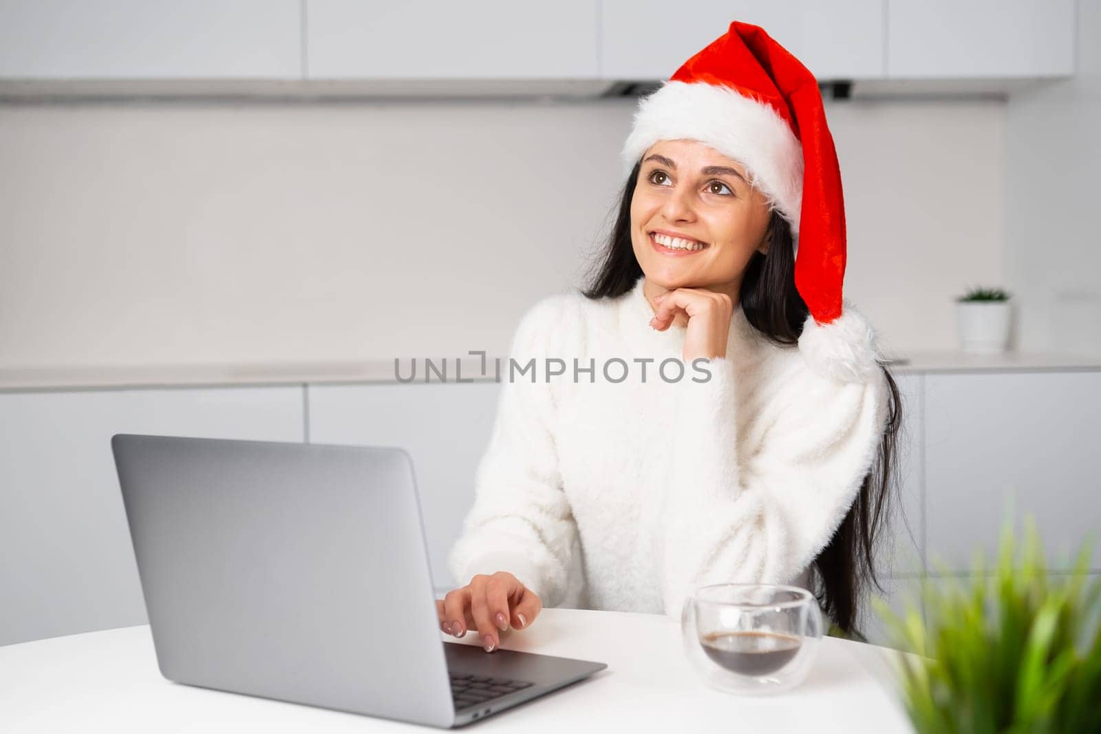 Exciting happy woman in Santa Claus hat imagines happy Christmas or New Year holidays. A woman works at home using her notebook before the party.