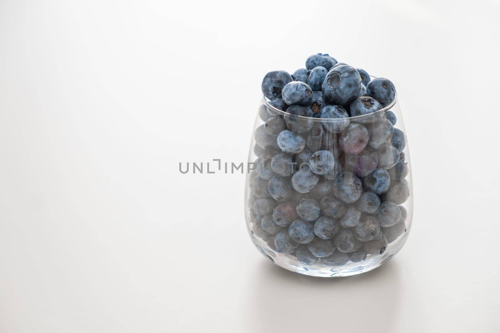 Blueberry in the glass standing on the white table. Healthy snack