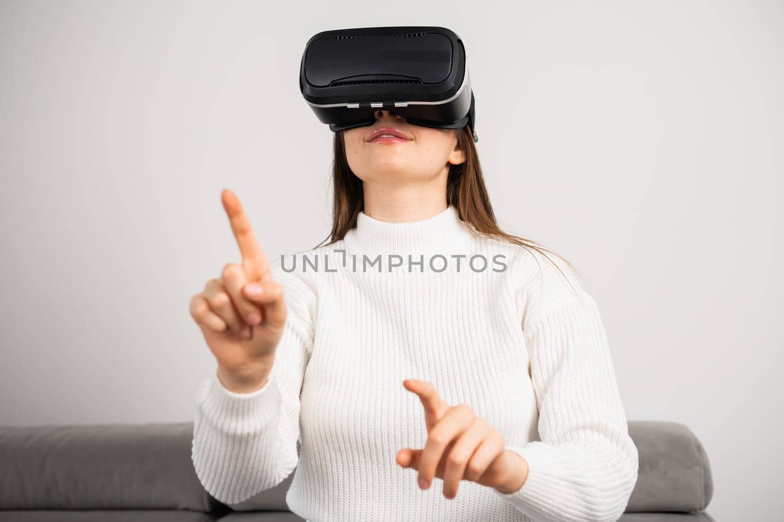 Young woman in VR glasses moves hand sitting on couch by vladimka