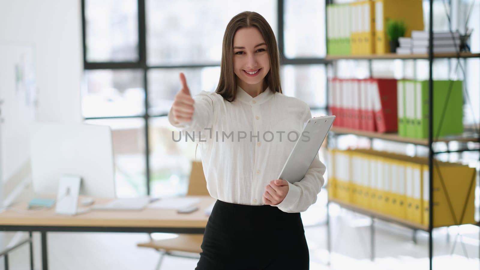 Businesswoman showing thumbs up at work in office. Successful career in business concept
