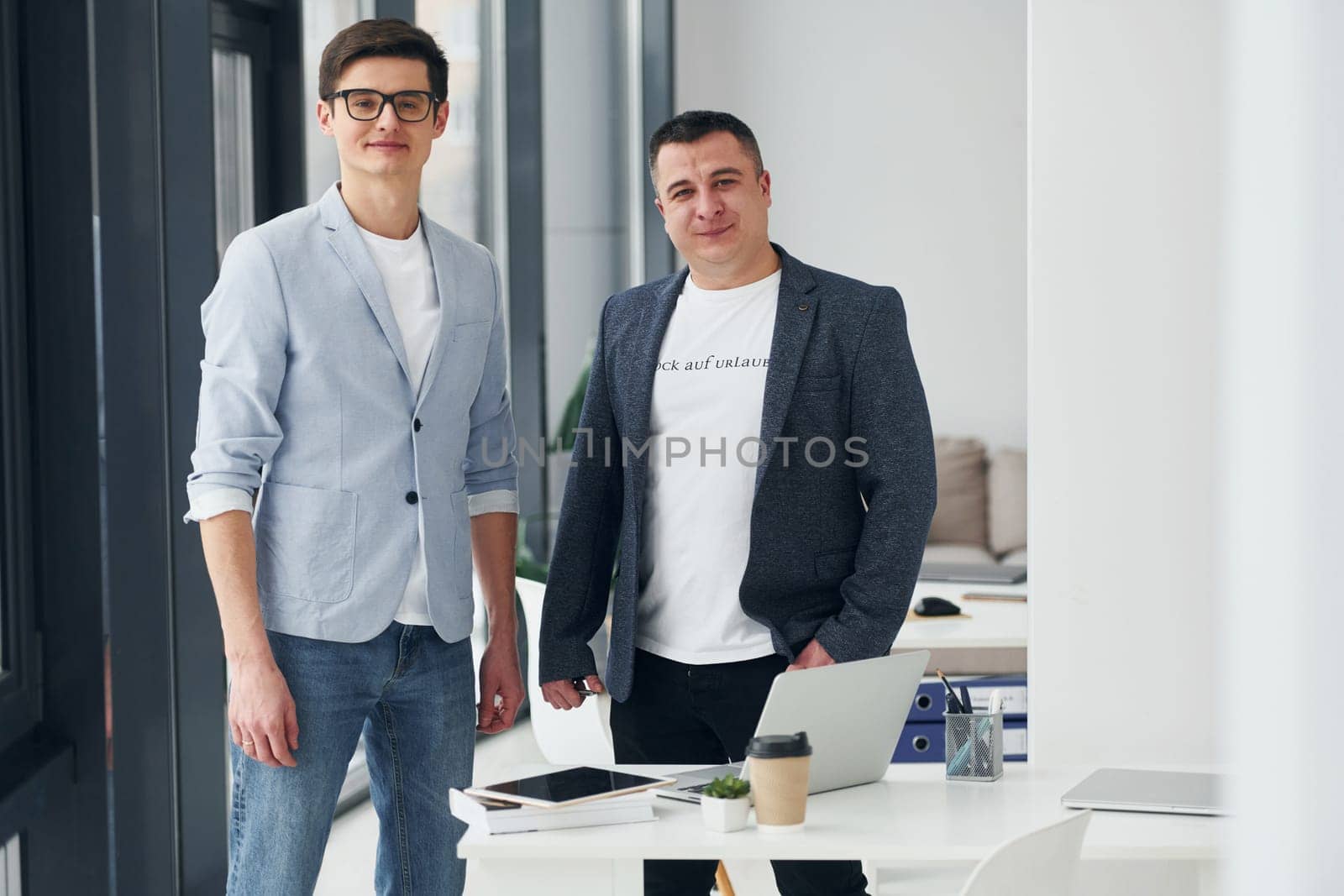 Young guy with adult man standing indoors in the office together.