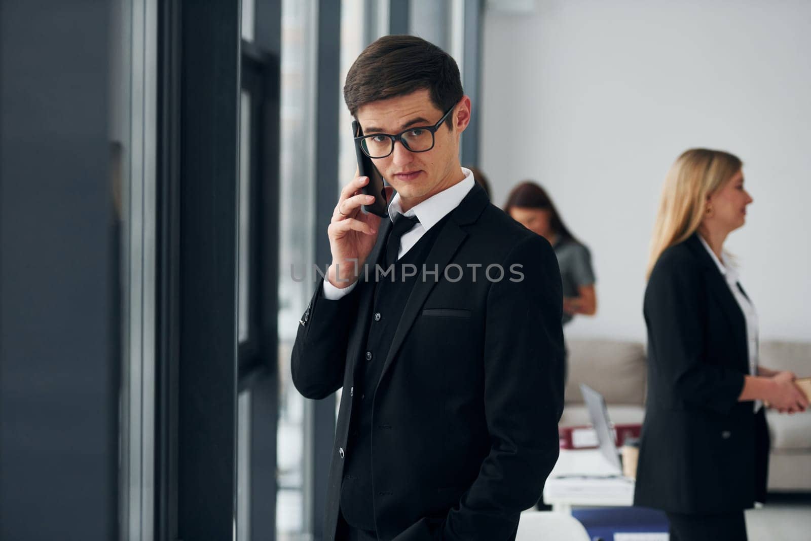 Young man with phone. Group of people in official formal clothes that is indoors in the office by Standret