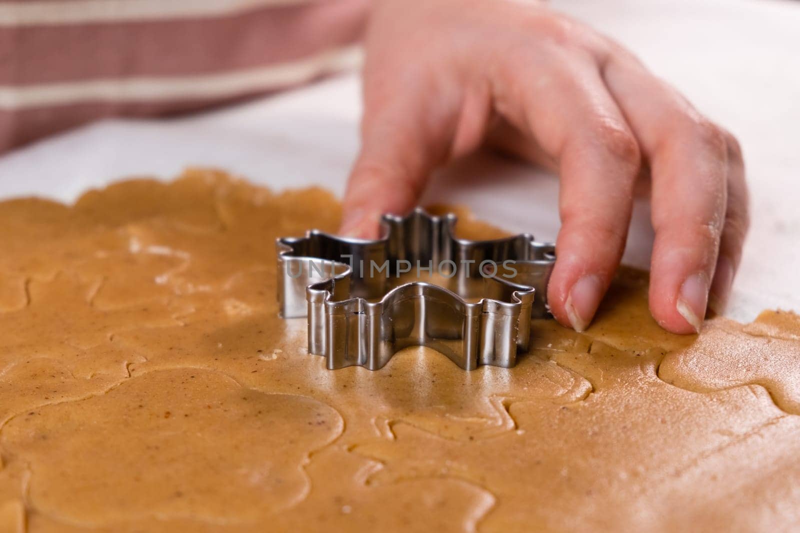 Close up woman hands cutting out cookies with metal mold from the shortcrust pastry. A metal forms in the form of snowflakes for making gingerbread for Christmas.