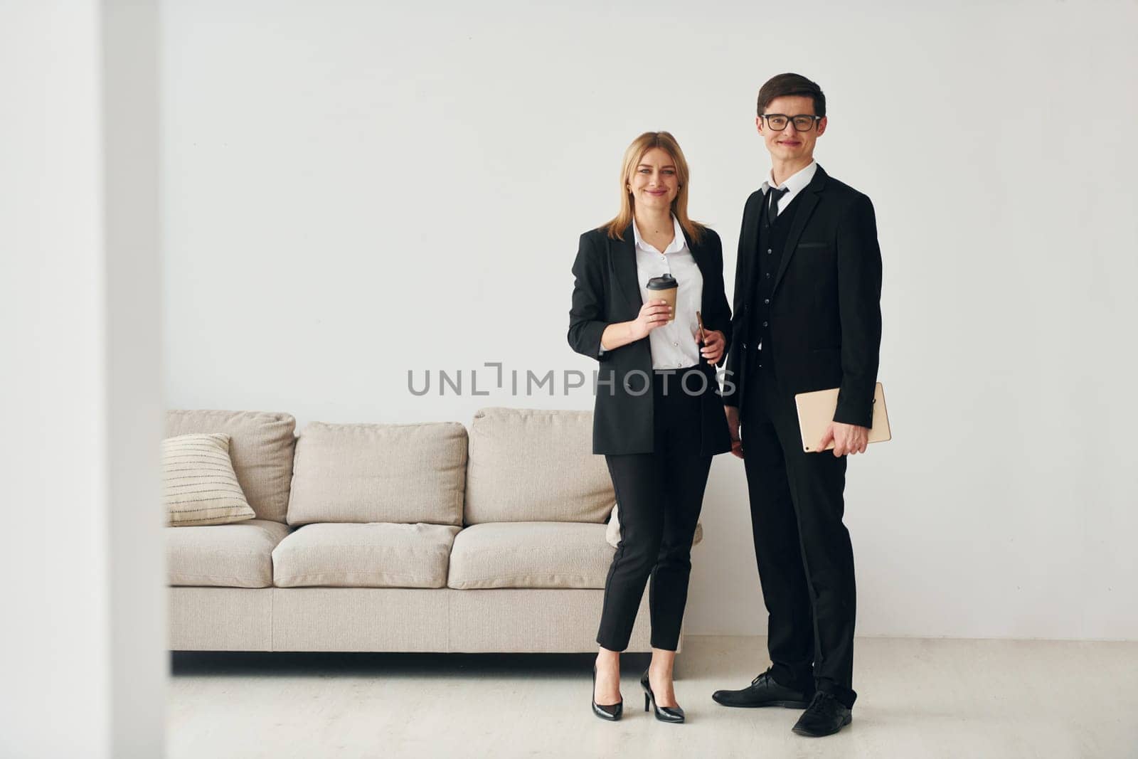 Young guys standing with woman indoors near sofa agaist white wall.