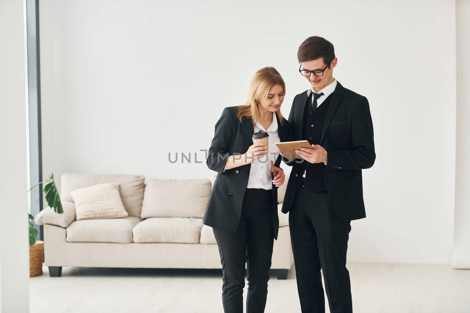 Young guys standing with woman indoors near sofa agaist white wall.