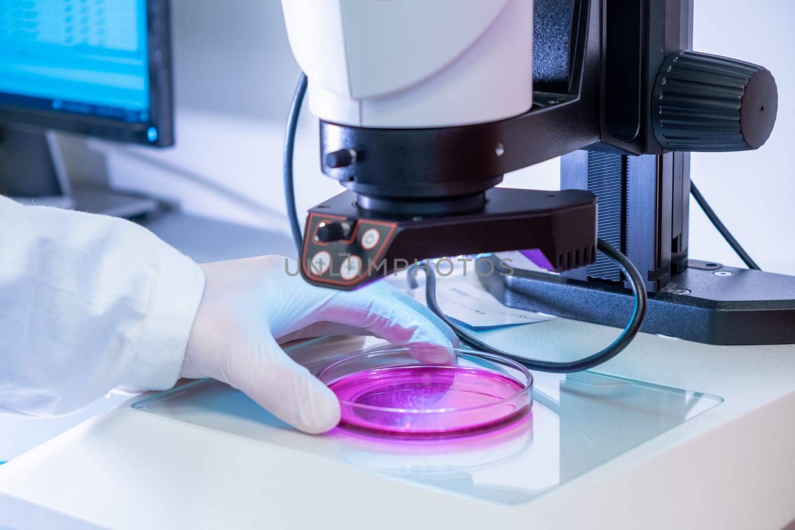 Scientist in latex gloves and lab coat putting samples under electronic microscope for testing or examination in microbiological or chemical laboratory.