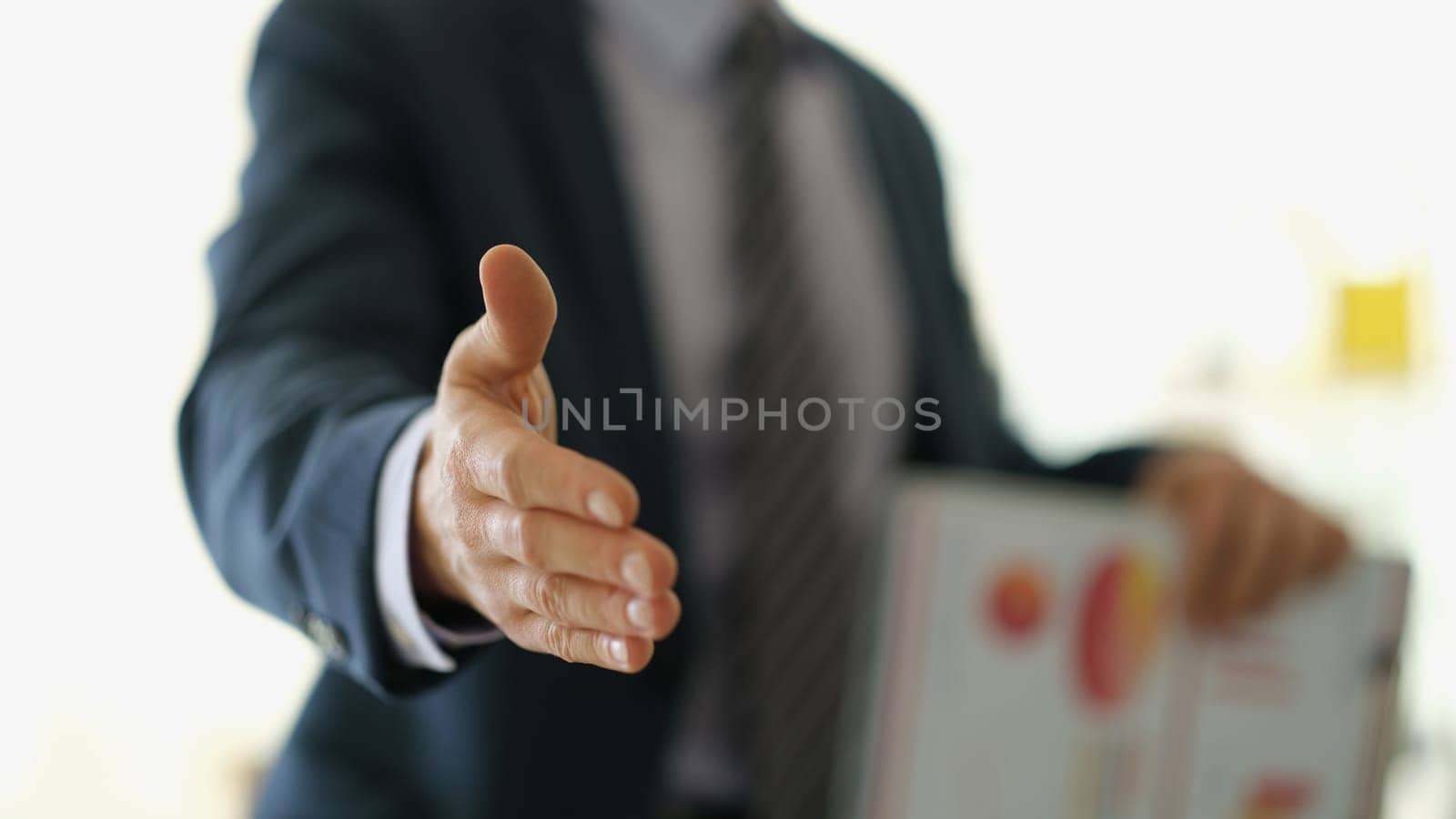 Businessman in suit with documents extending hand to partner for handshake closeup. Team work concept