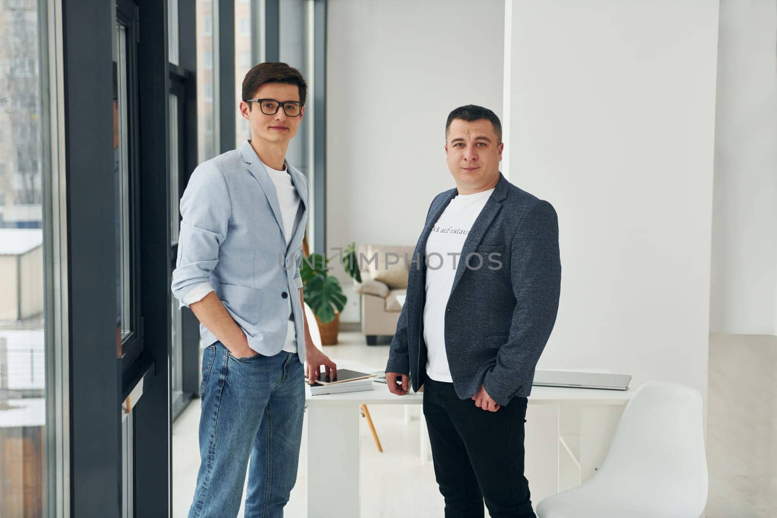 Young guy with adult man standing indoors in the office together.