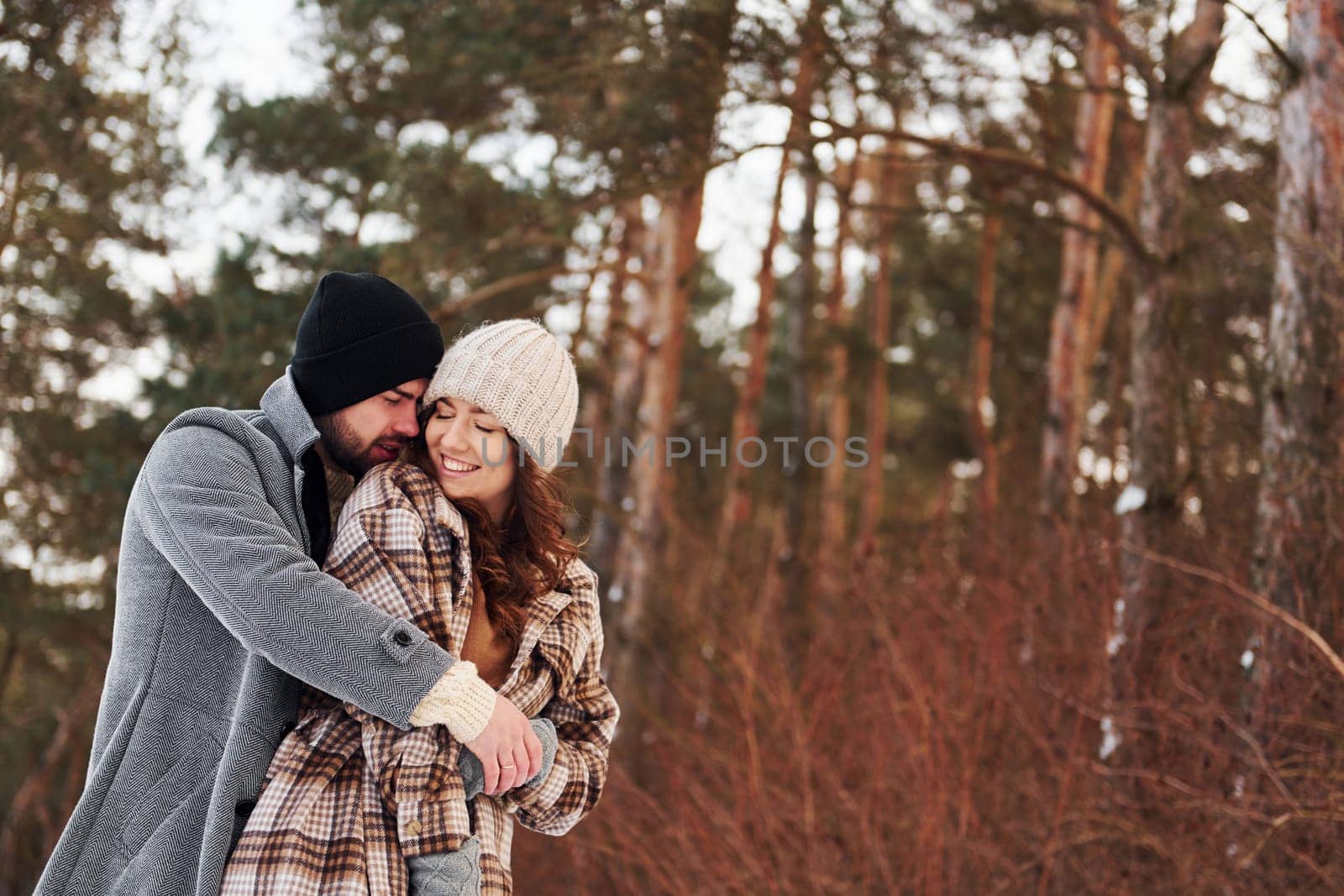 Cheerful couple have a walk in the winter forest at daytime.