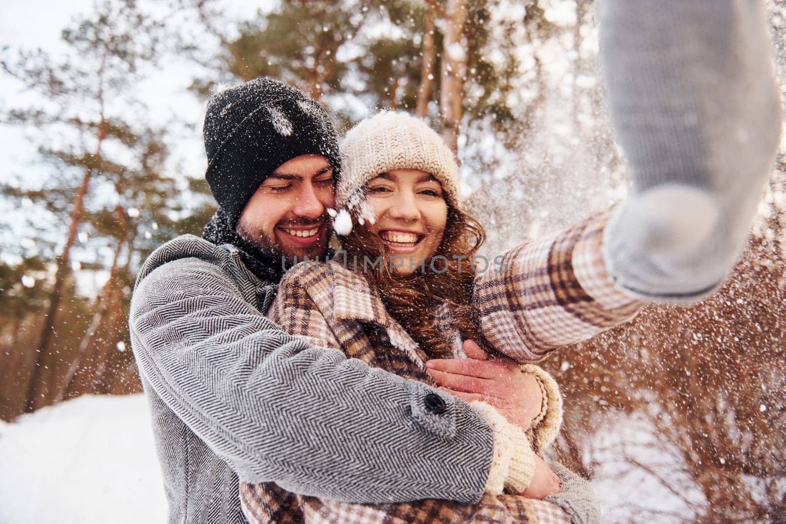 Cheerful couple have a walk in the winter forest at daytime.