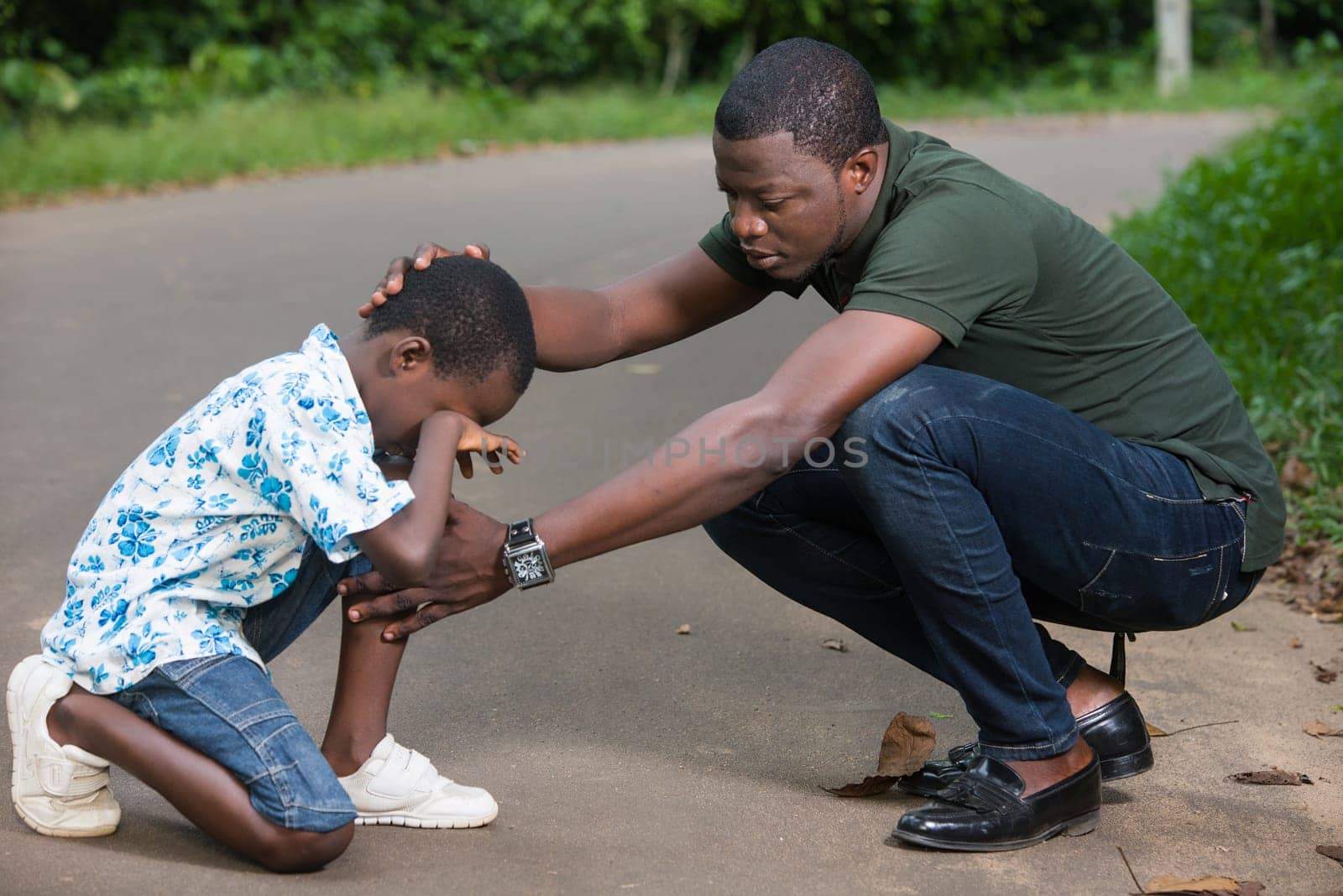 a young man crouched in a park air to calm his son who is crying.