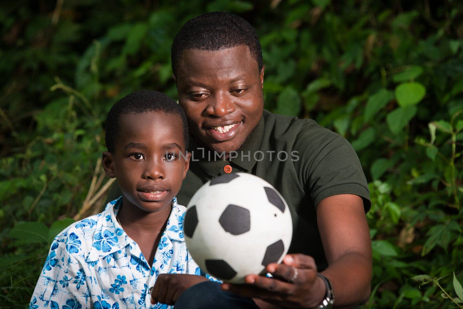 a young family sitting in a park with a ball smiling.