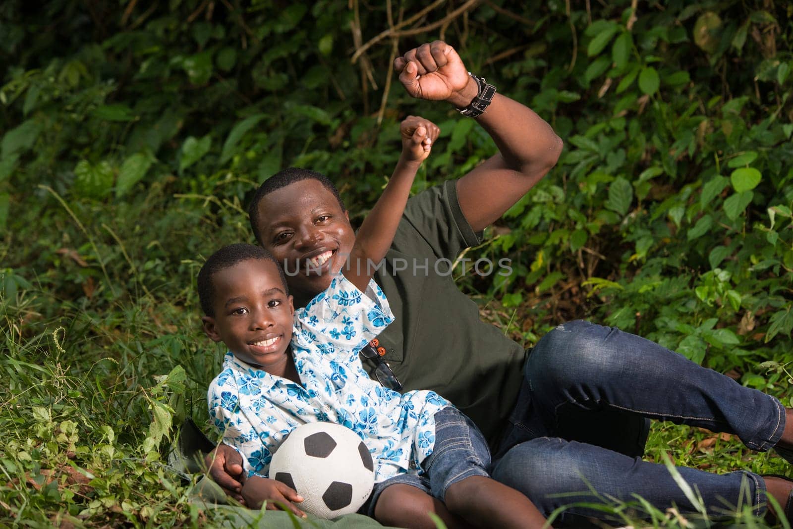 young man lying in a park with his son clenched fists and look at the camera smiling.