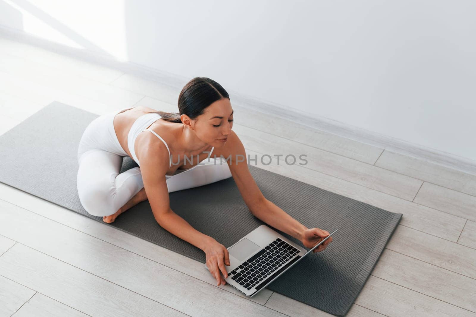 On yoga mat. Young caucasian woman with slim body shape is indoors at daytime.